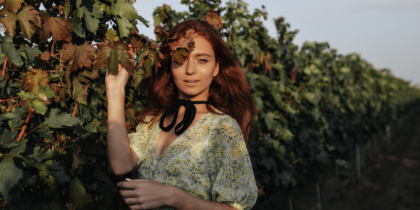 Trendy girl with long red hairstyle and black bandage on neck in light fashionable green clothes lo Trendy girl with long red hairstyle and black bandage on neck in light fashionable green clothes looking into camera on background of vineyards..